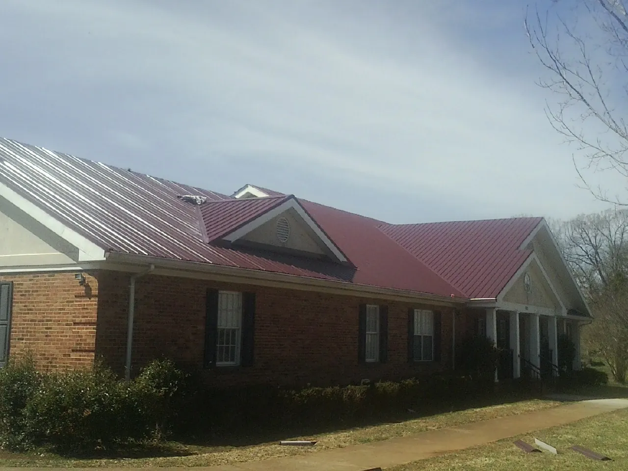Red metal roof with gabled entries on a long brick building, from a Hail Damage Roof Repair job in Erin