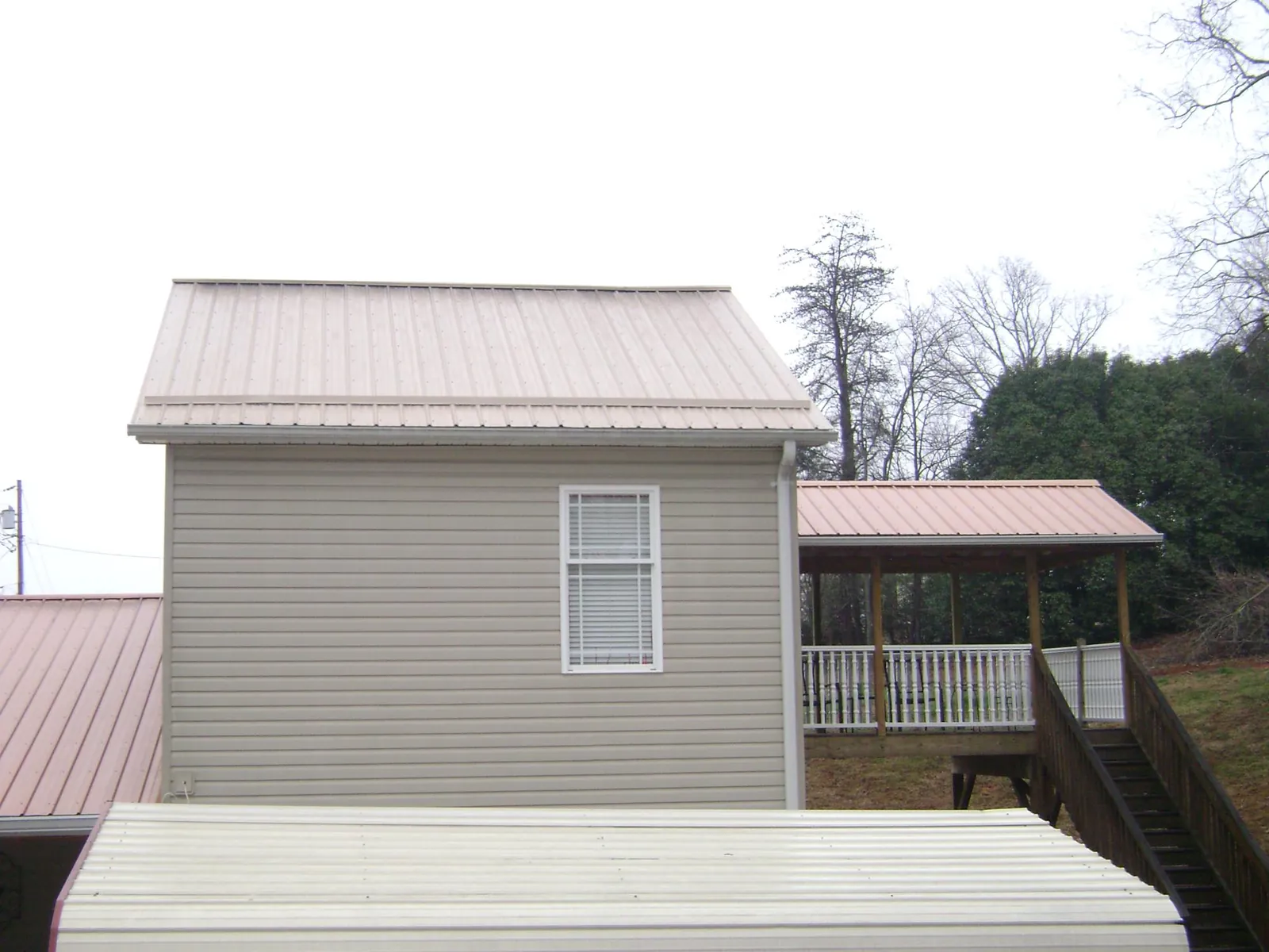 Tan metal roofs on a two story addition and attached porch, from a Roof Replacement job in Erin